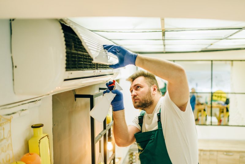 Repairman in uniform cleans the air conditioner